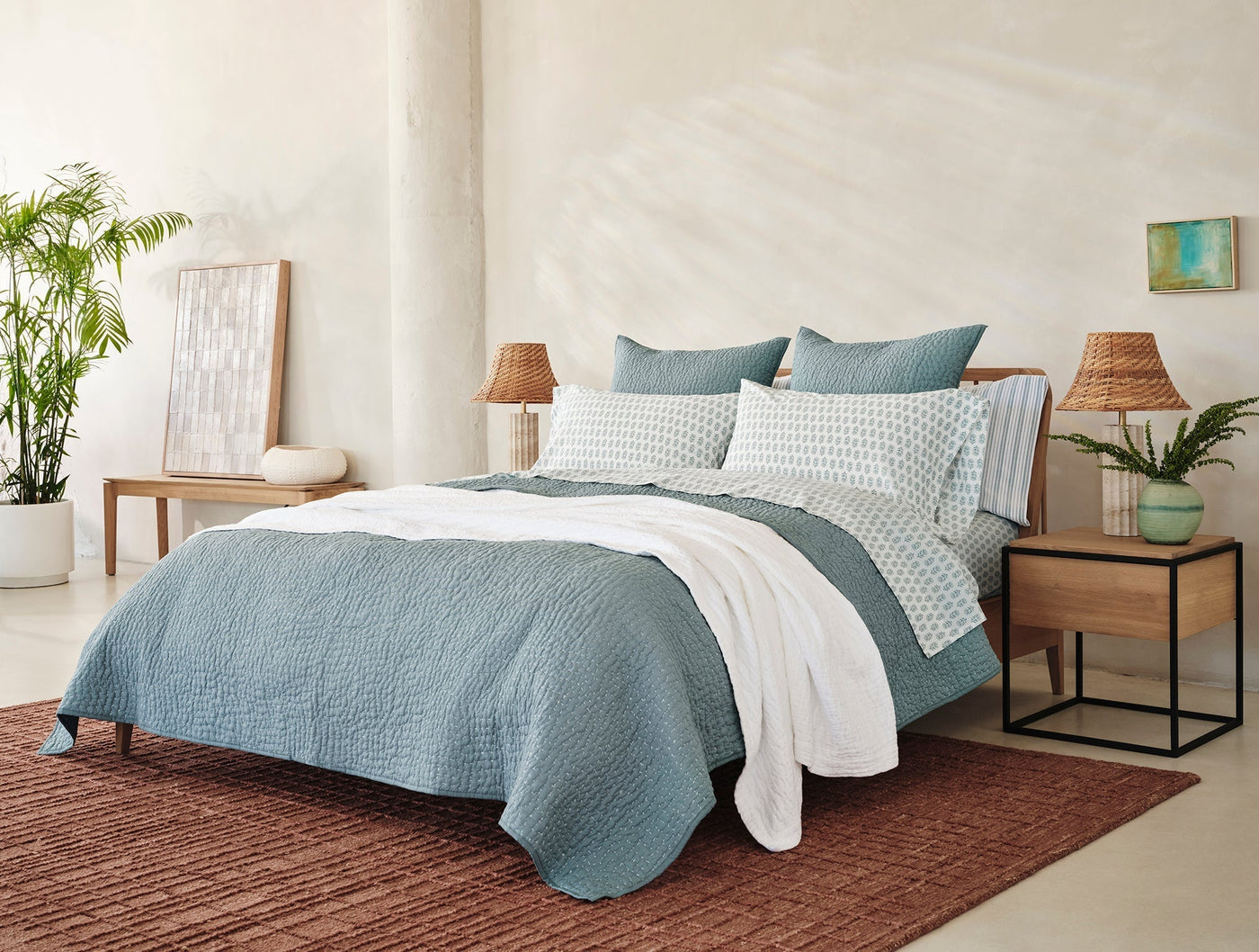 Coyuchi Pebbled Handstitched quilt in teal styled on bed with white sheets in bright bedroom.