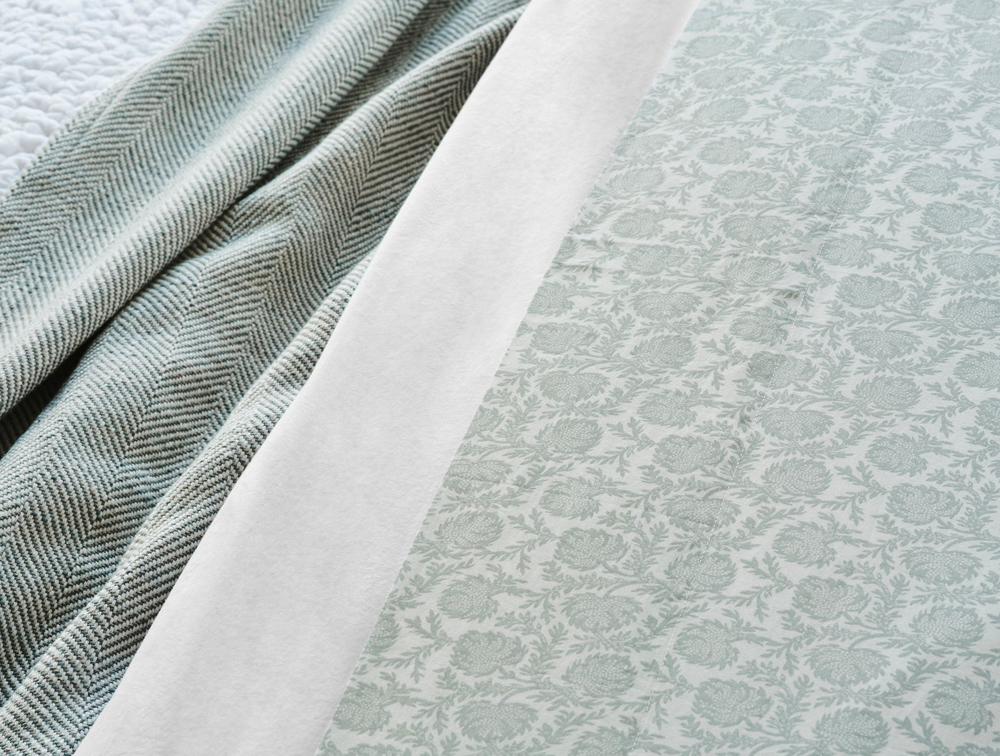 Close-up of sage floral print percale sheet with herringbone blanket and white flat sheet layered.