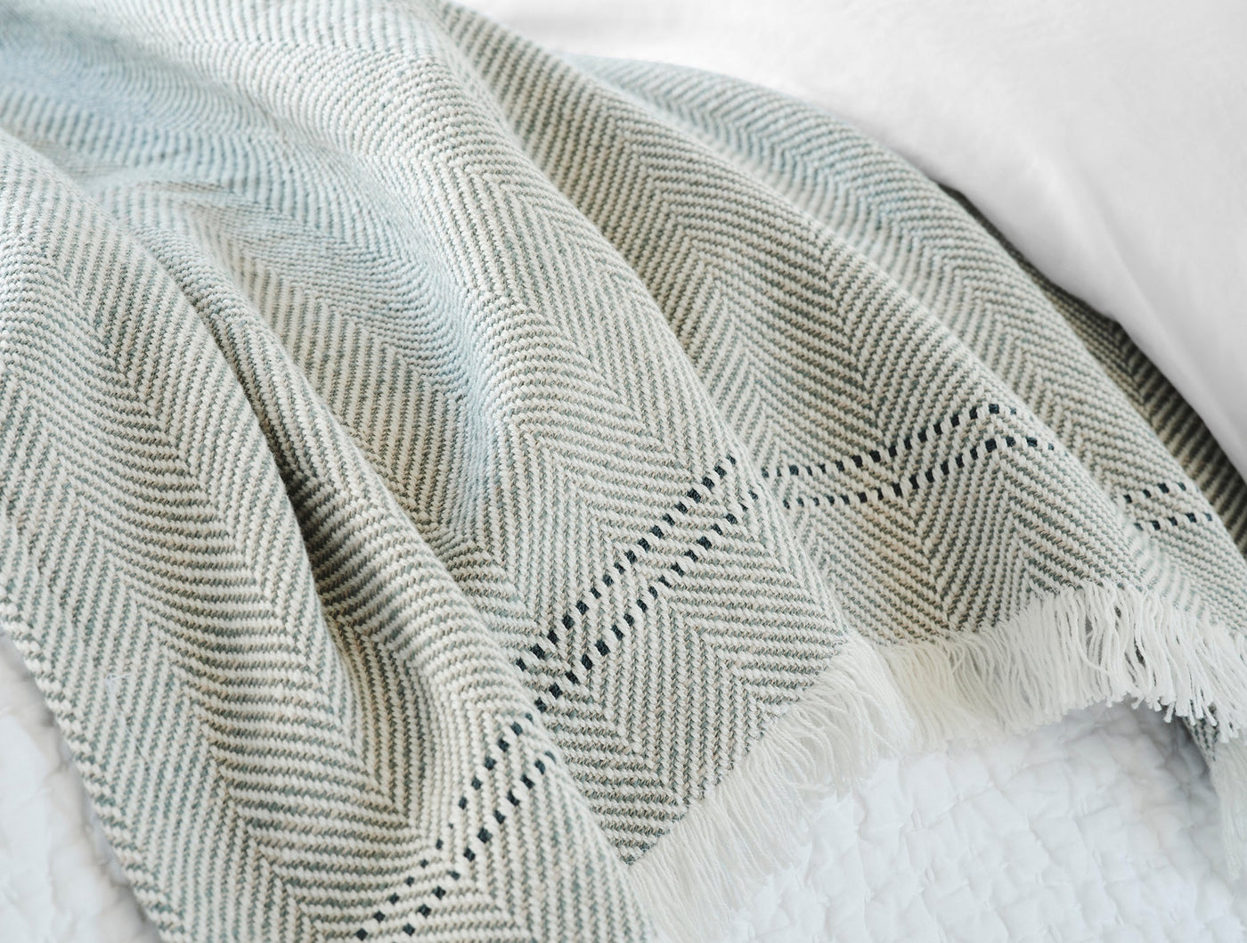 Close-up of Coyuchi Canyon throw's sage herringbone weave and fringe edge detail.