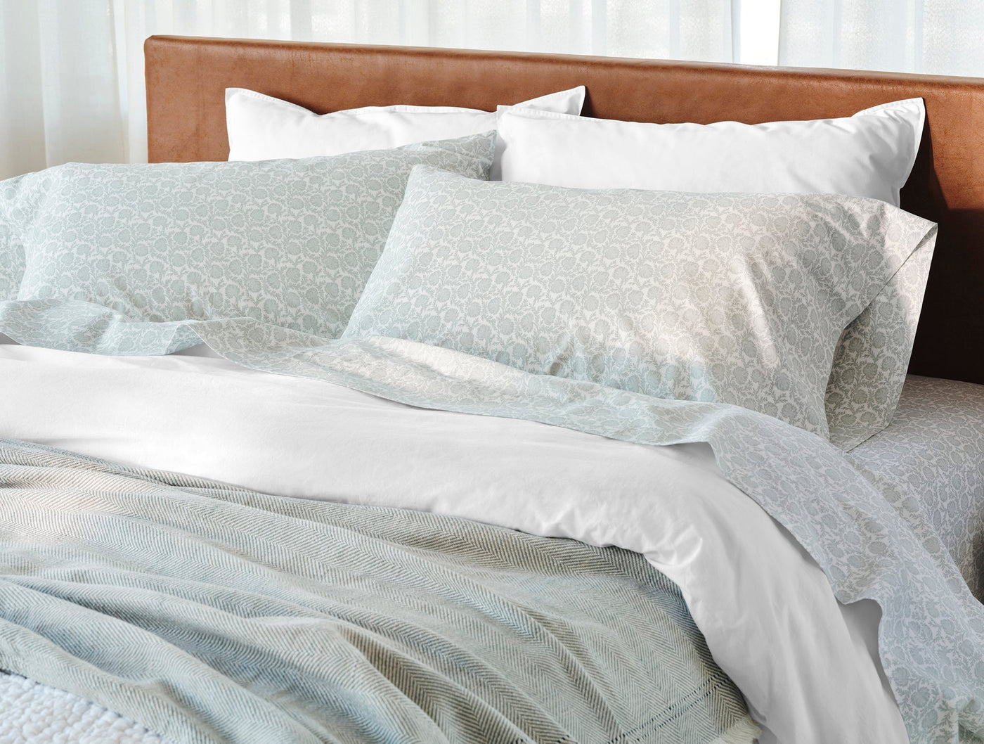 Sage floral-print percale shams layered with white pillows on a styled bed.