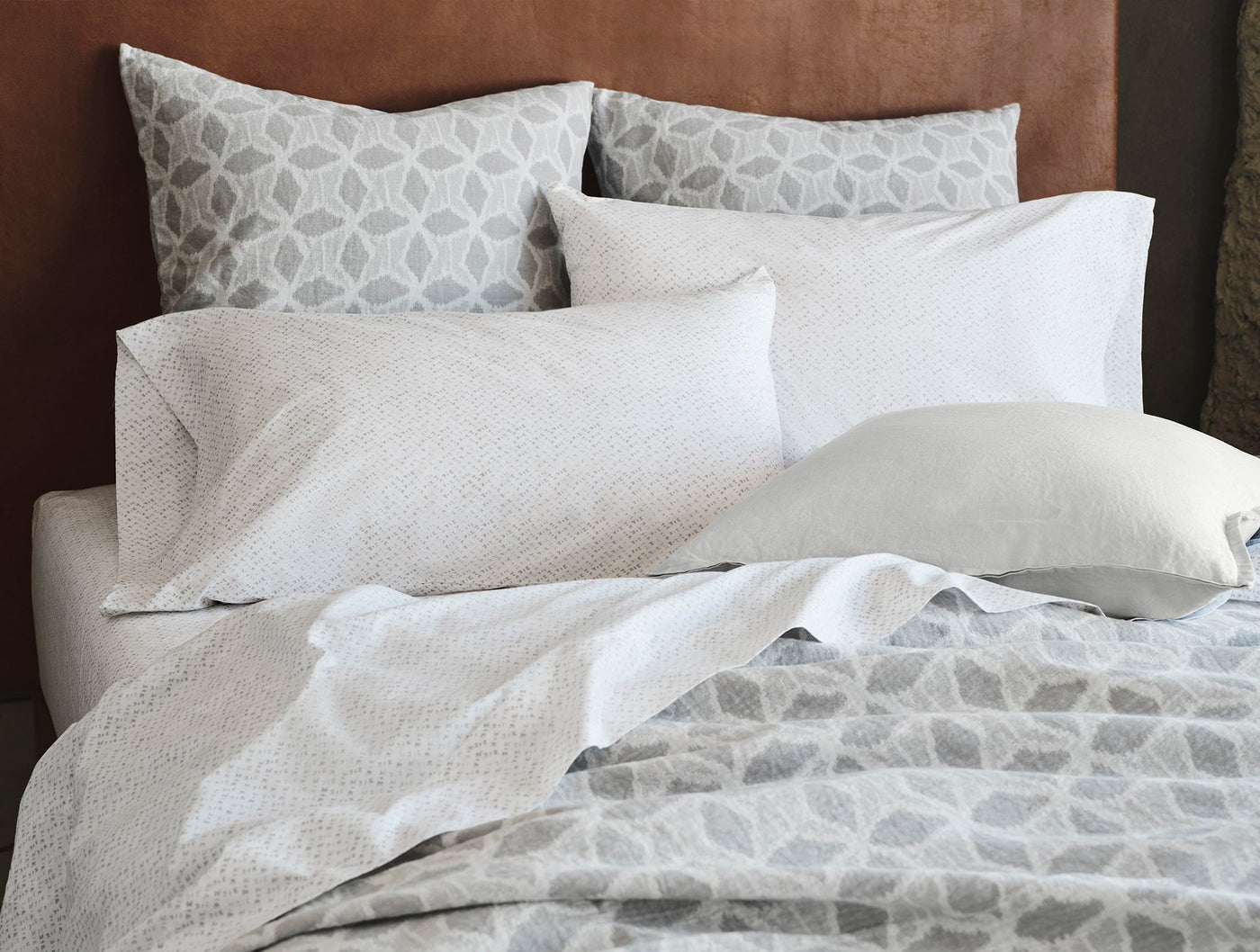 Close-up of Coyuchi Palomar blanket draped over bed with layered white and grey bedding.