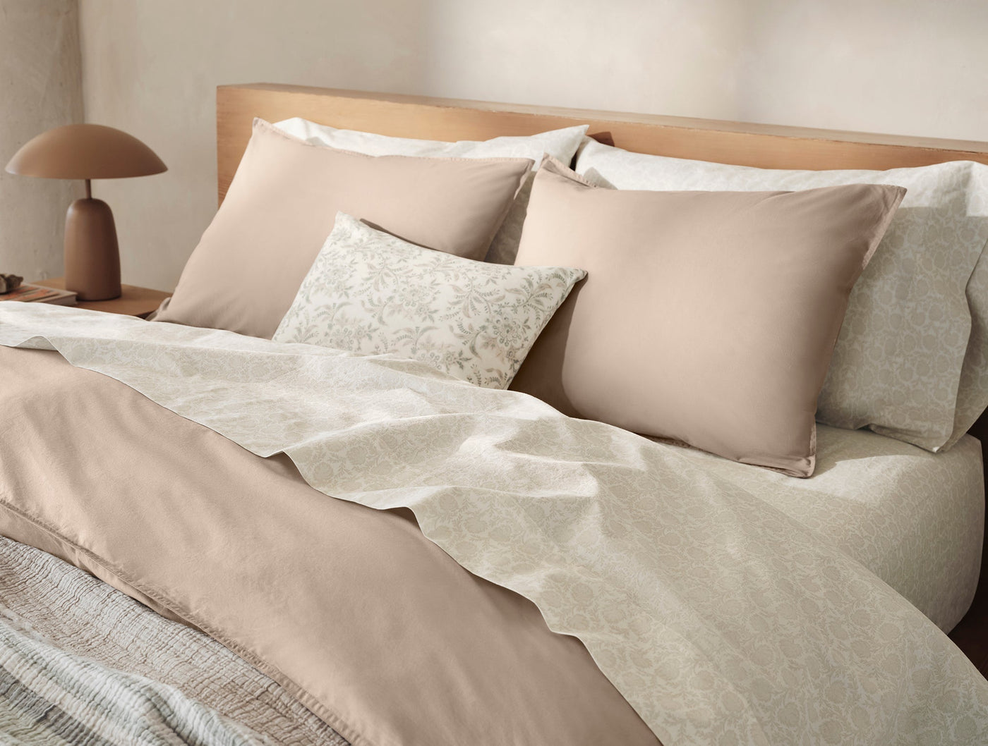 Marguerite Print decorative pillow styled on a bed with blush duvet and layered neutral linens.