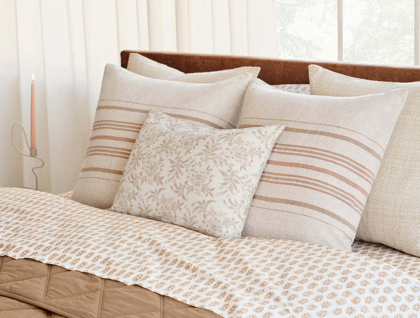 Coyuchi Marguerite Print pillow styled on bed with striped and linen cushions in warm neutrals.