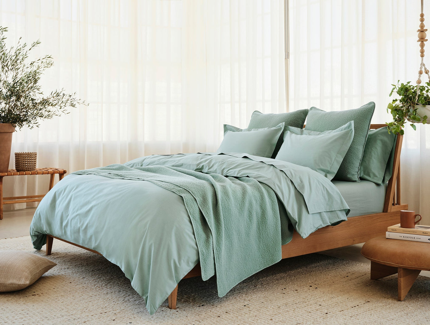 Sage green percale sheet set on a wood-frame bed in a light-filled room.