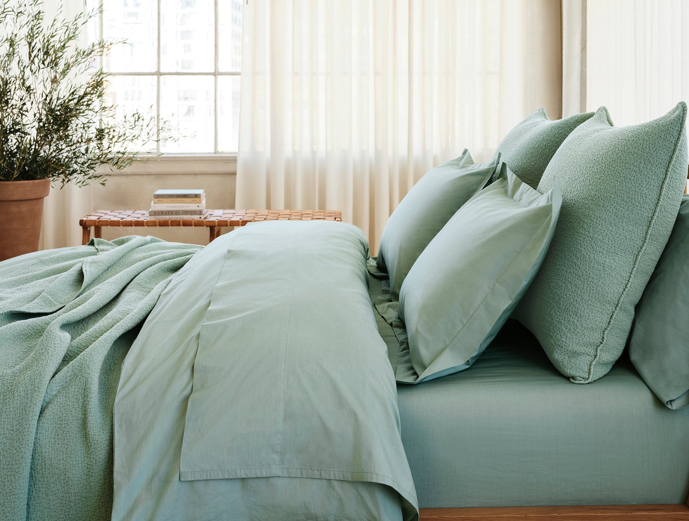 Coyuchi Refined Percale duvet cover in sage, styled on bed with layered pillows.