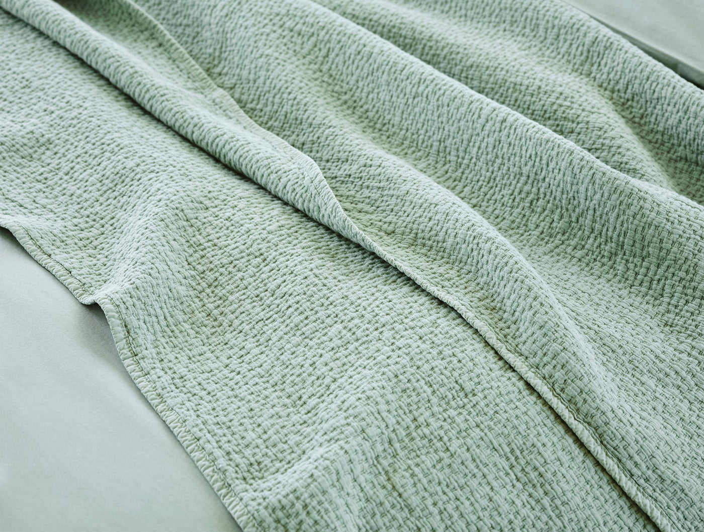 Close-up of sage Coyuchi Cascade Matelasse blanket showing textured weave and soft drape.