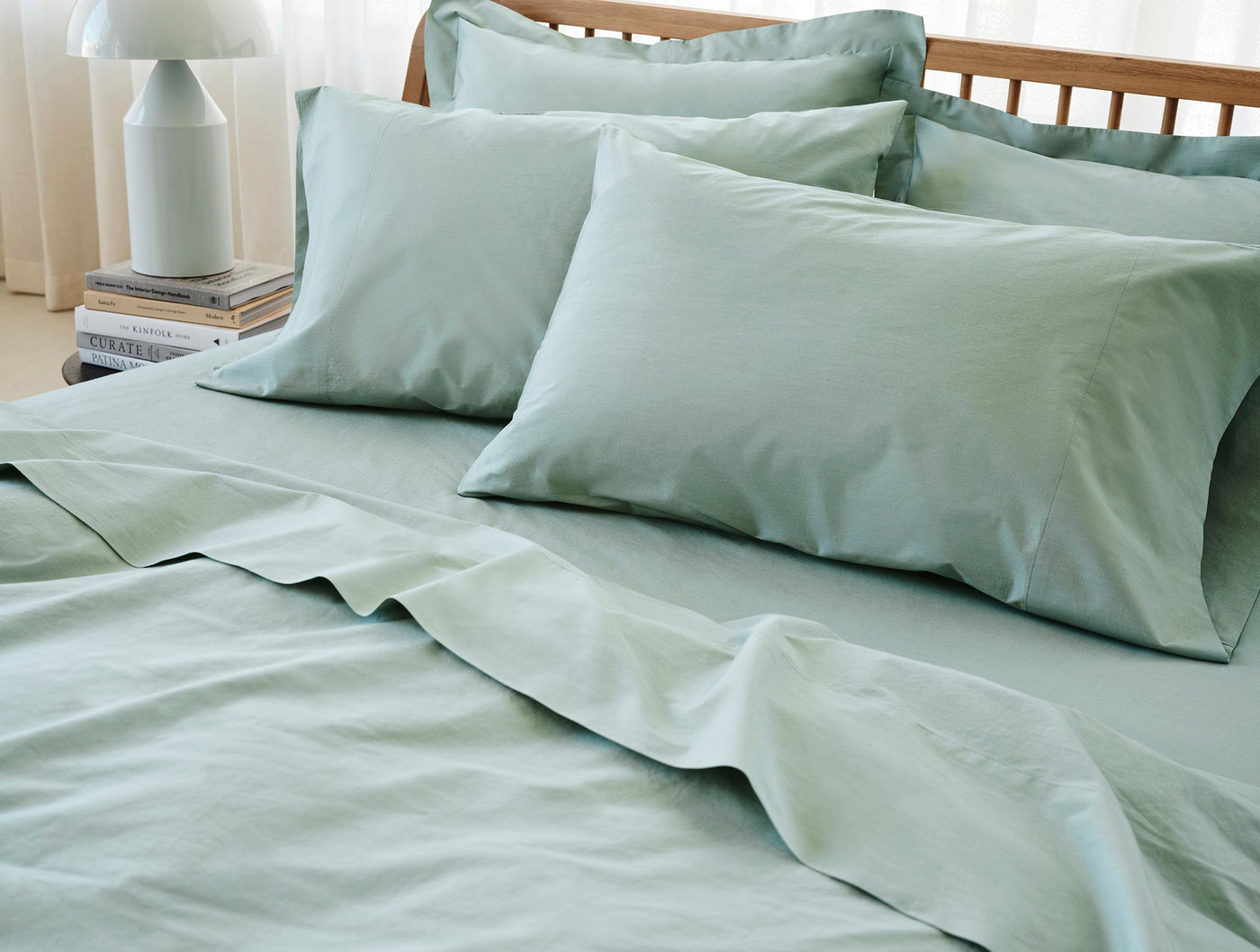 Close-up of sage green Coyuchi Refined Percale pillowcases styled on a made bed.
