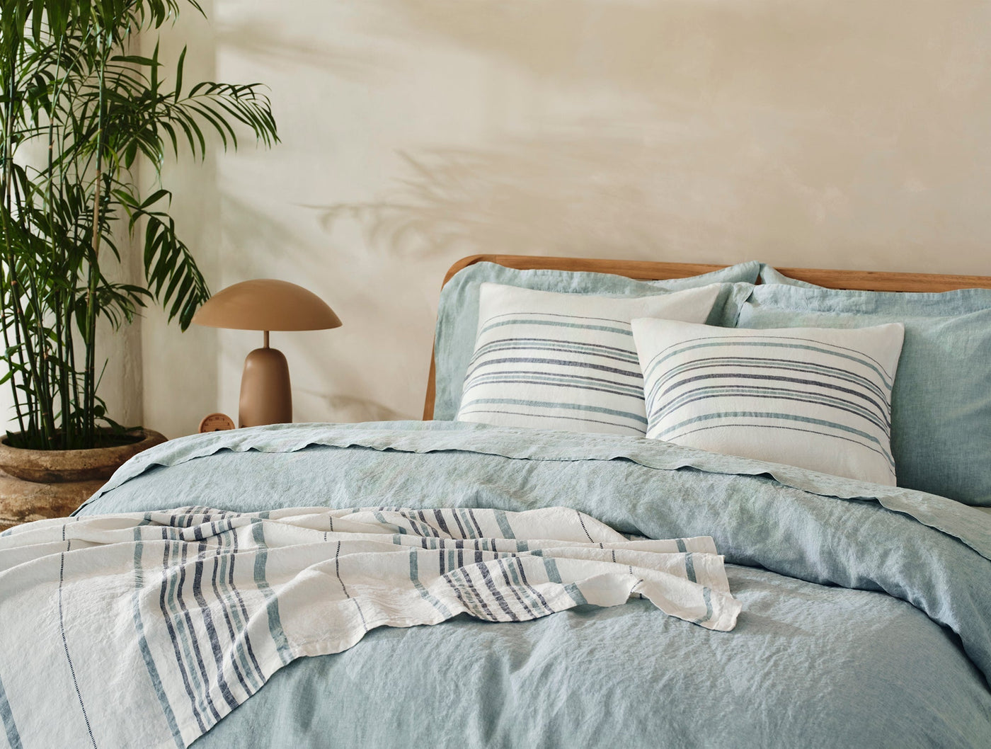 Mojave Linen decorative pillow styled on a sage linen bed with navy stripe accents.