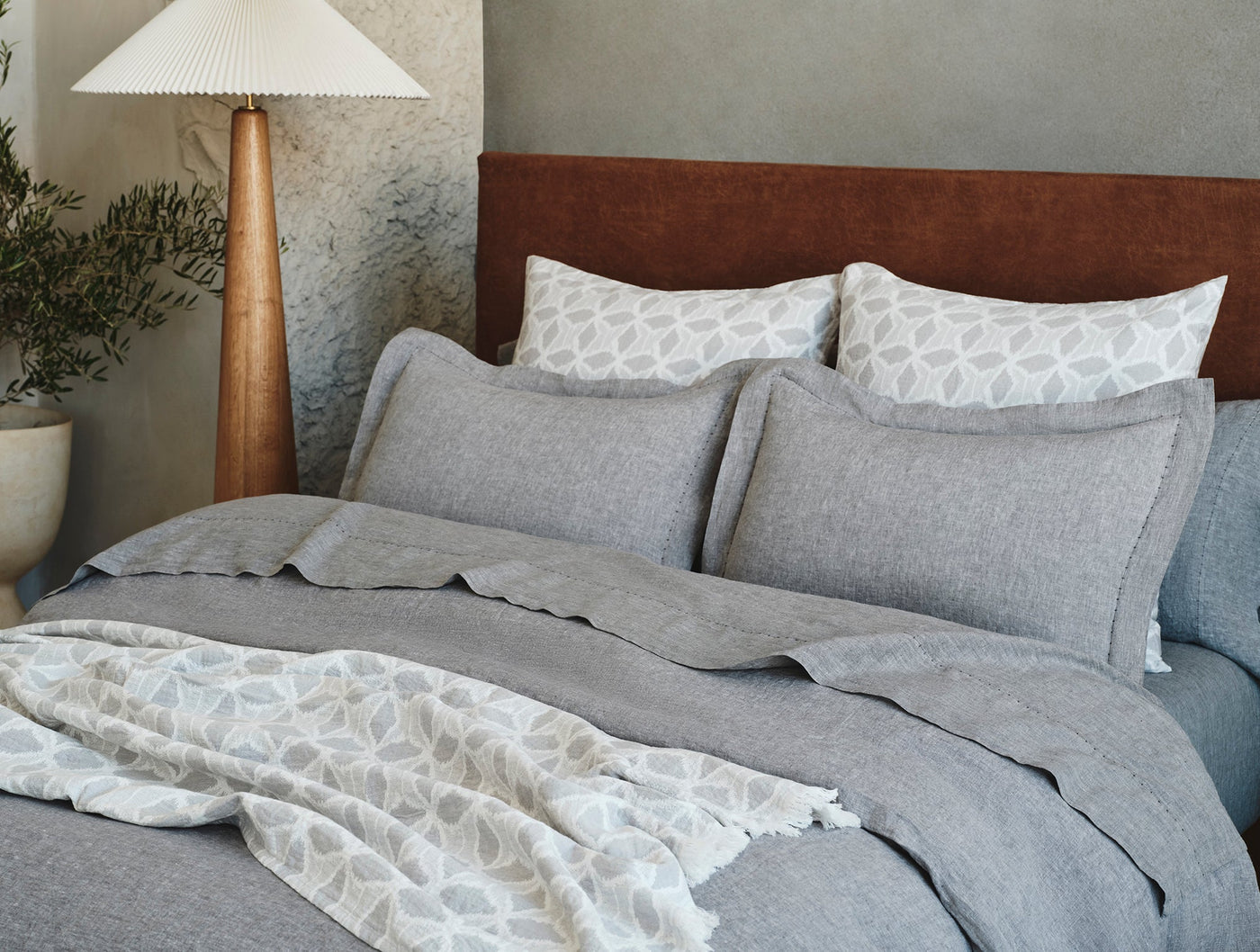 Coyuchi Relaxed Linen duvet cover in slate grey styled on bed with leaf-print pillows.