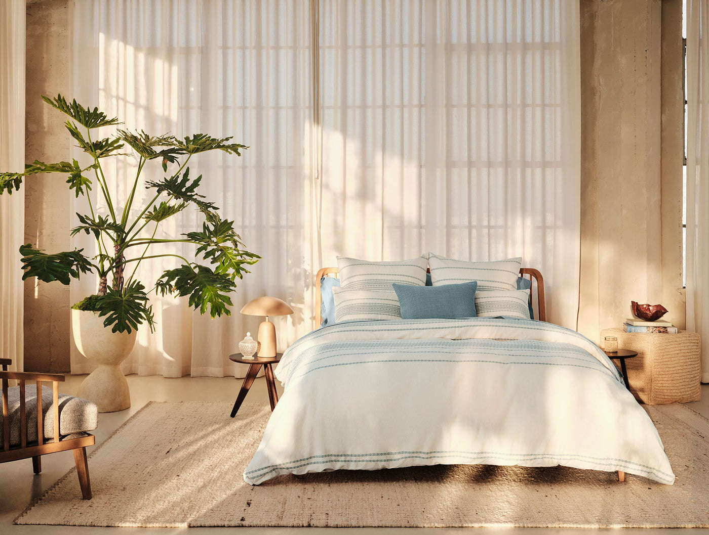 Ivory duvet cover with blue stripes styled on a bed in a sun-lit natural bedroom.