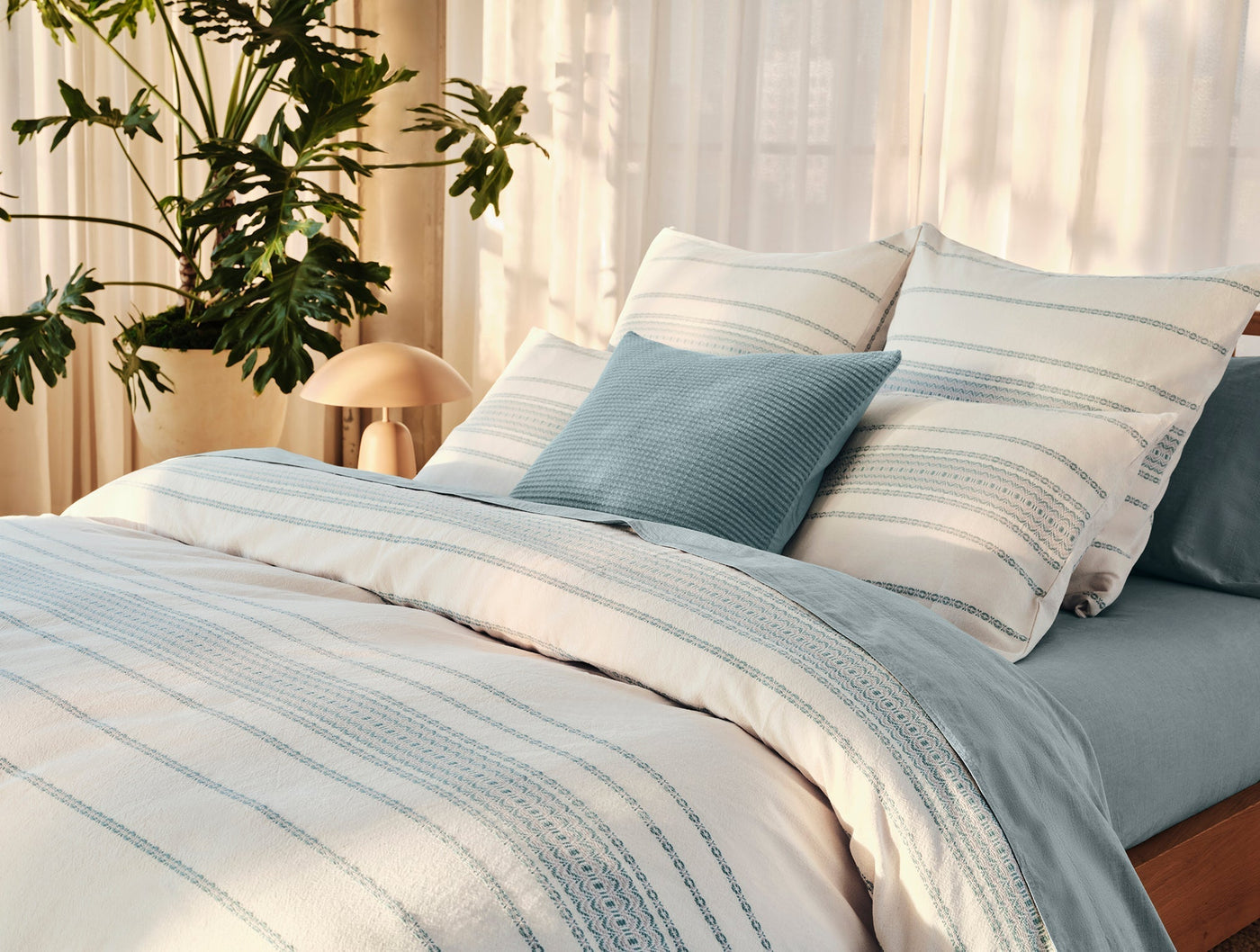 Styled bedroom scene showing dusty blue ribbed Coyuchi throw pillow among striped bedding.