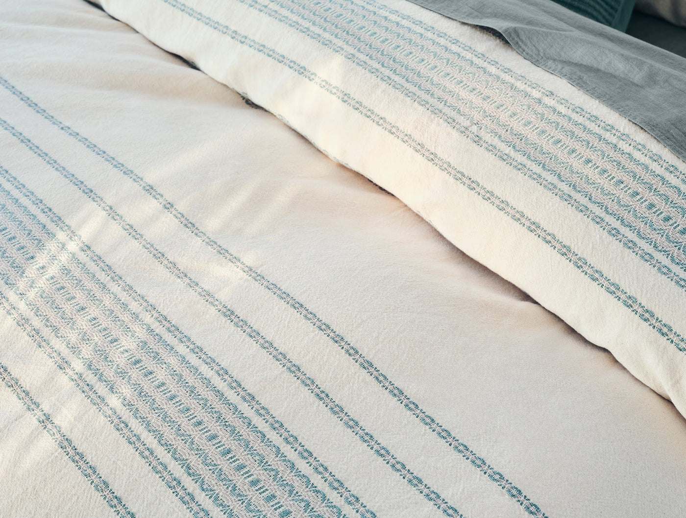 Close-up of ivory duvet cover with teal woven rippled stripes, showing fold detail.