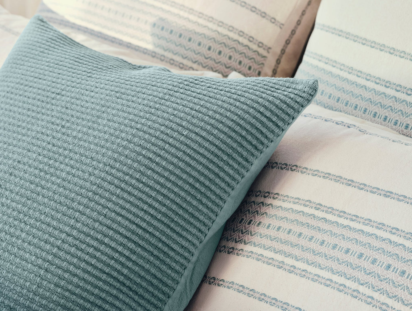 Close-up of Coyuchi Marshall pillow in teal ribbed texture against patterned bedding.