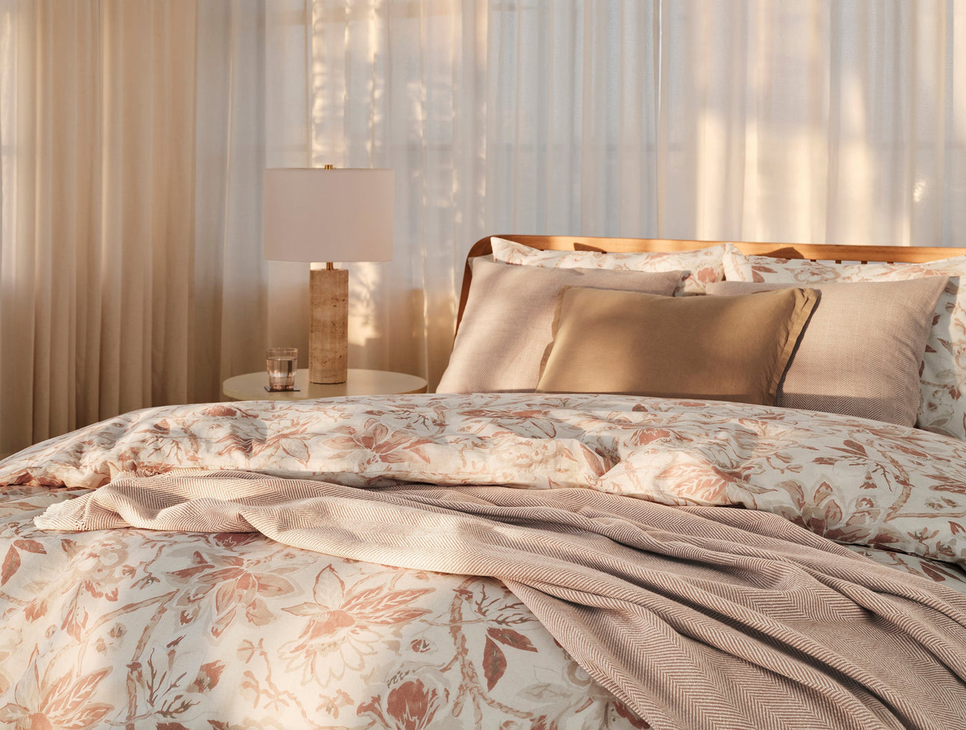 Dusty rose woven throw draped over floral bedding in a sun-dappled bedroom setting.