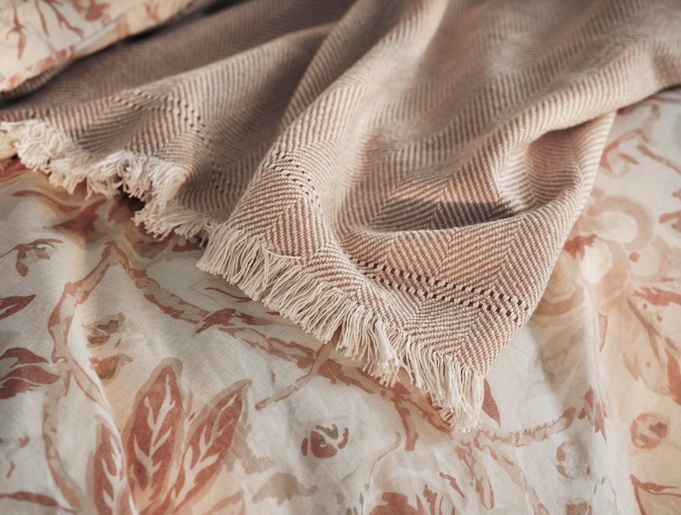 Close-up of Coyuchi Canyon throw fringe hem, herringbone weave in warm blush tones.