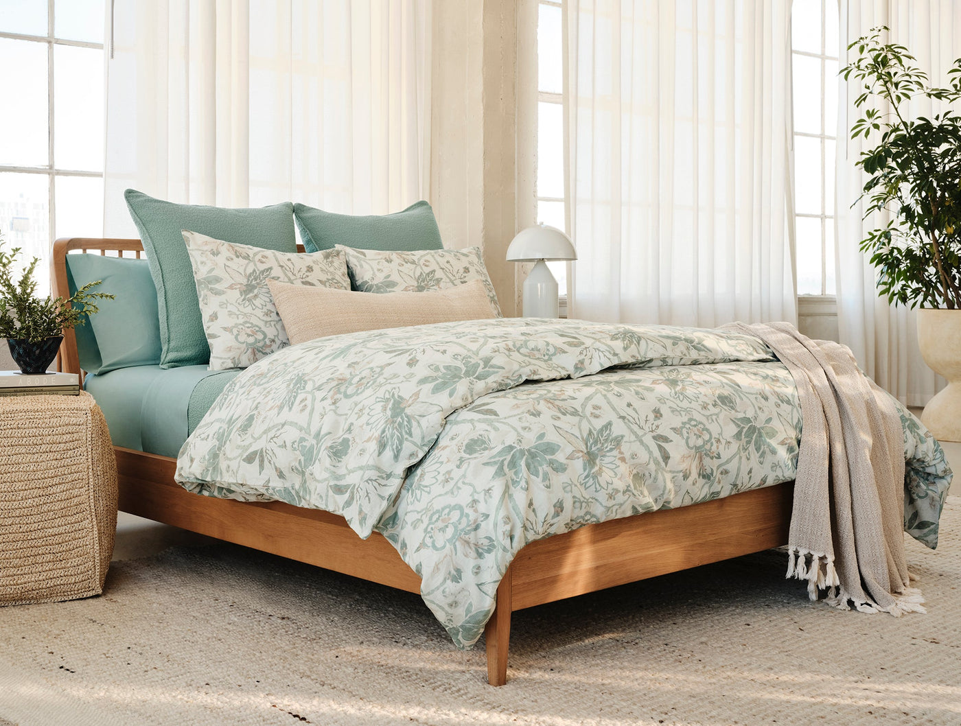 Sage green duvet and floral-printed bedding styled on a wood bed in a bright bedroom.