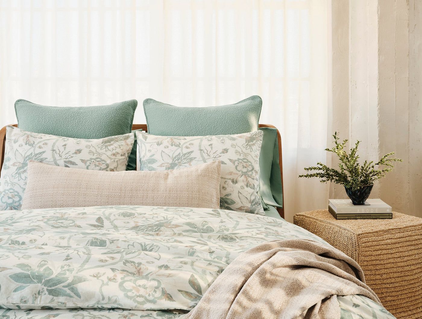 Sage green decorative pillow styled on a bed with floral bedding and neutral accessories.
