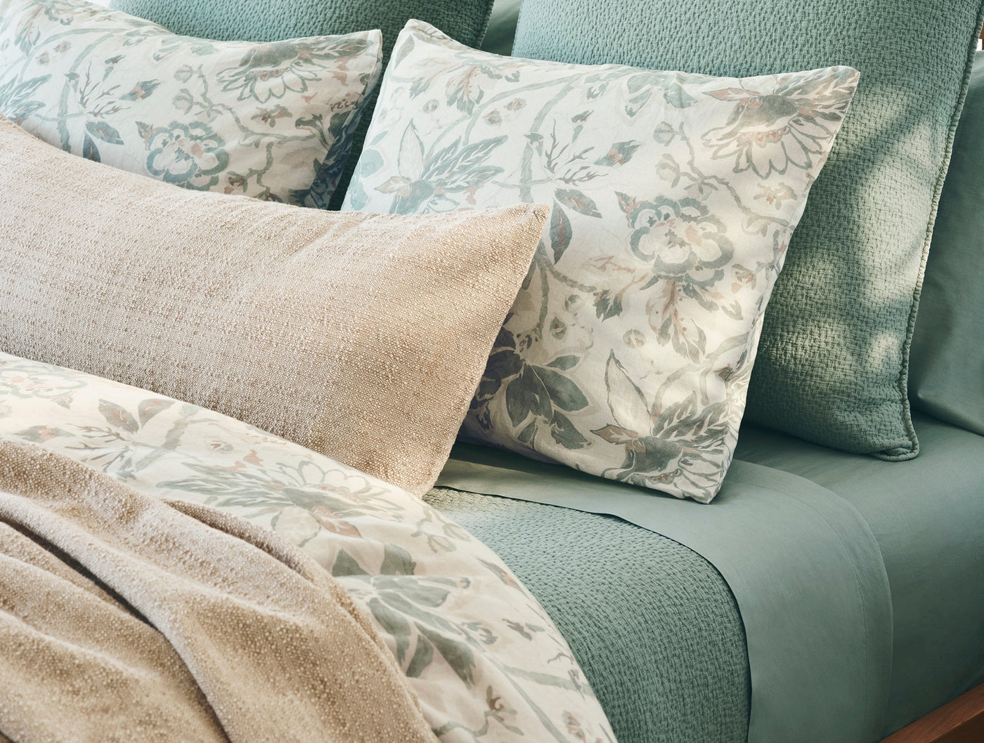 Floral print shams layered with sage solid bedding and a natural lumbar pillow.