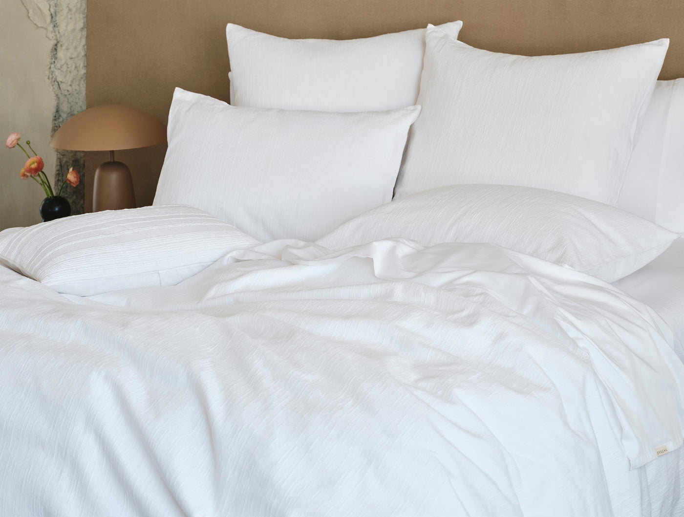 White textured pillow sham on a styled bed with layered white bedding and warm amber accents.