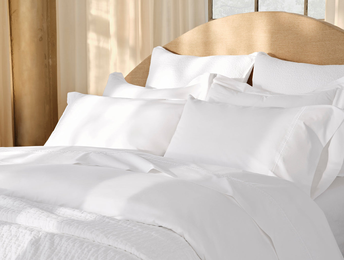 Close-up of white Coyuchi Trailing Embroidered sheet set styled on a sunlit bed.