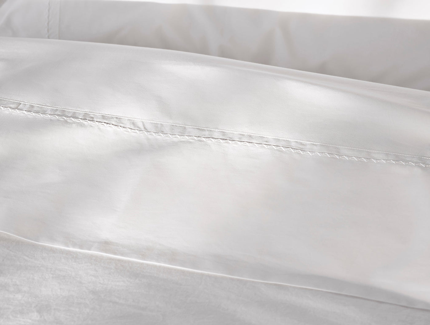 Close-up of white sheet hem with delicate trailing embroidered detail on sateen fabric.