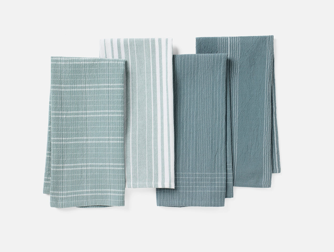 Coyuchi Fillmore kitchen towels in four muted teal patterns, flat lay arrangement.