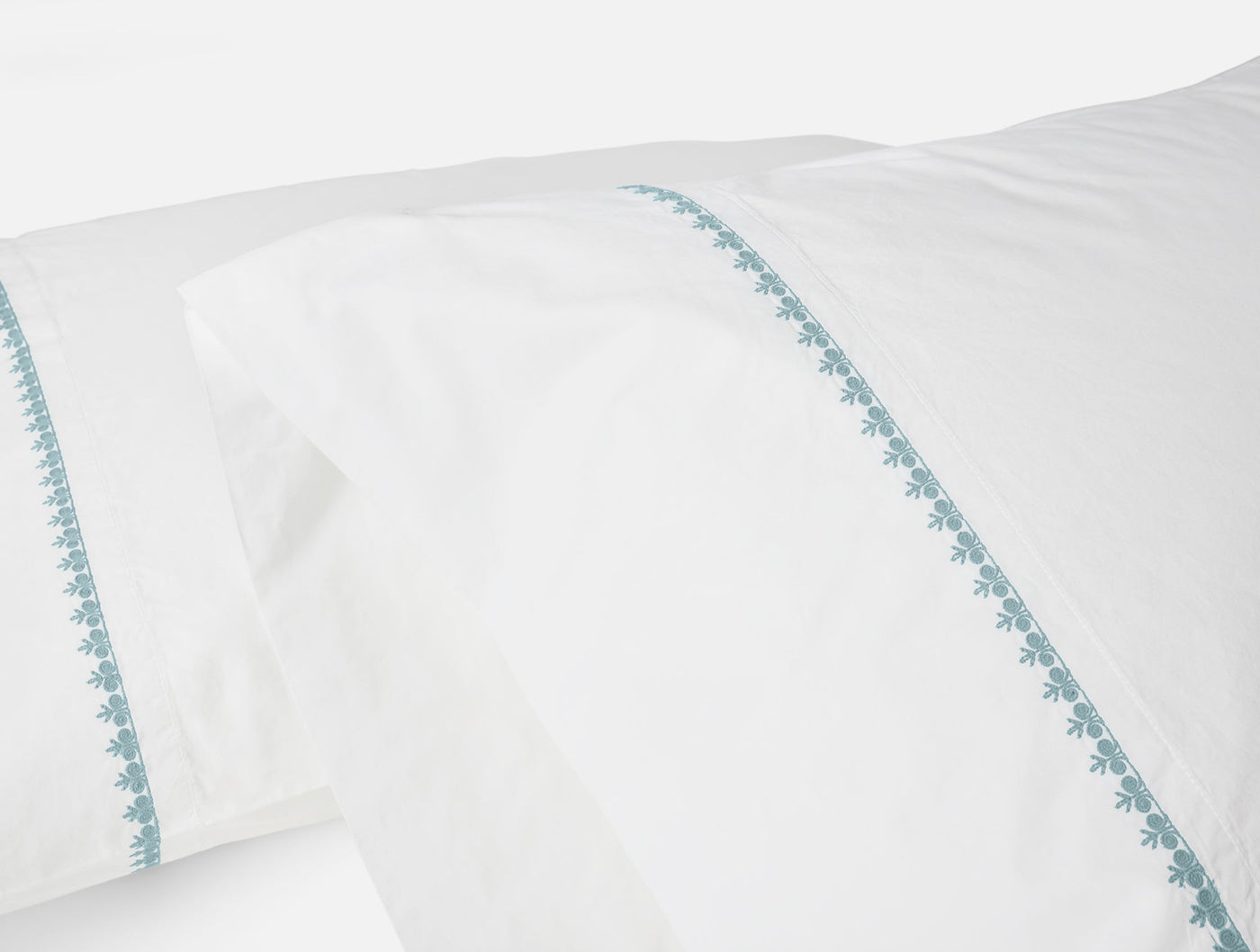 Close-up of teal floral embroidered border on white Coyuchi Floret pillowcase.