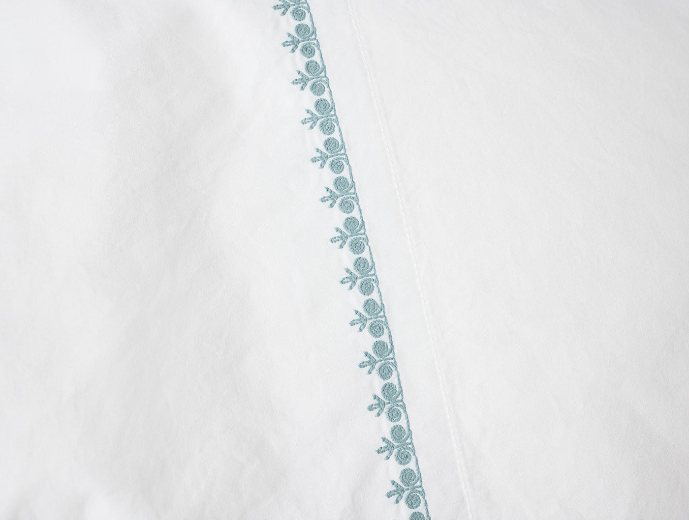 Close-up of teal floral embroidered border on white Coyuchi Floret pillowcase.