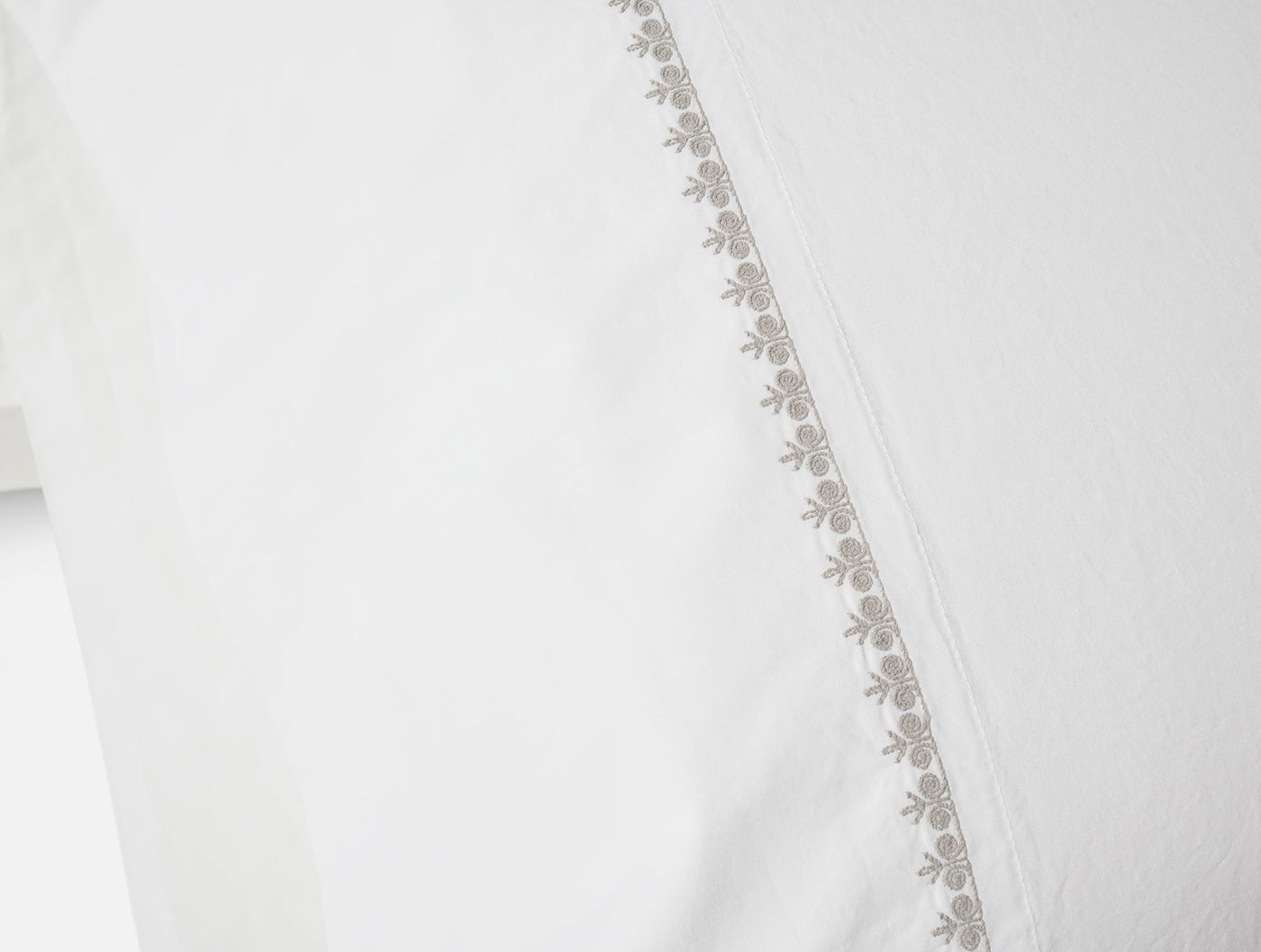 Close-up of taupe floral embroidered hem on white Coyuchi Floret sheet.