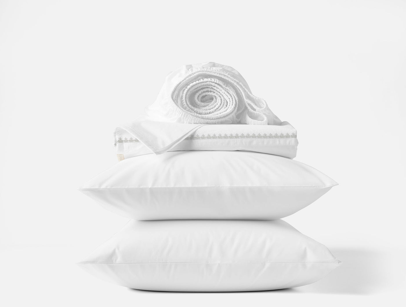Close-up of white Coyuchi Floret sheet set with embroidered trim, stacked on two pillows.