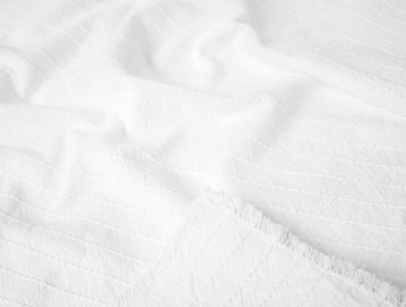 White textured cotton napkin close-up showing fringe trim and woven stripe detail.