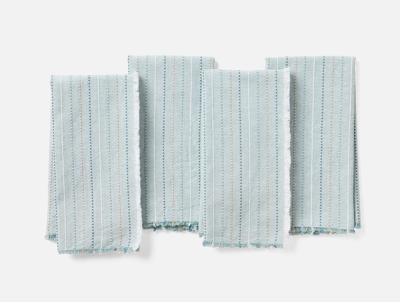 Four Coyuchi Fringe Stripe napkins laid flat, pale aqua with dotted stripe pattern and fringe hem.