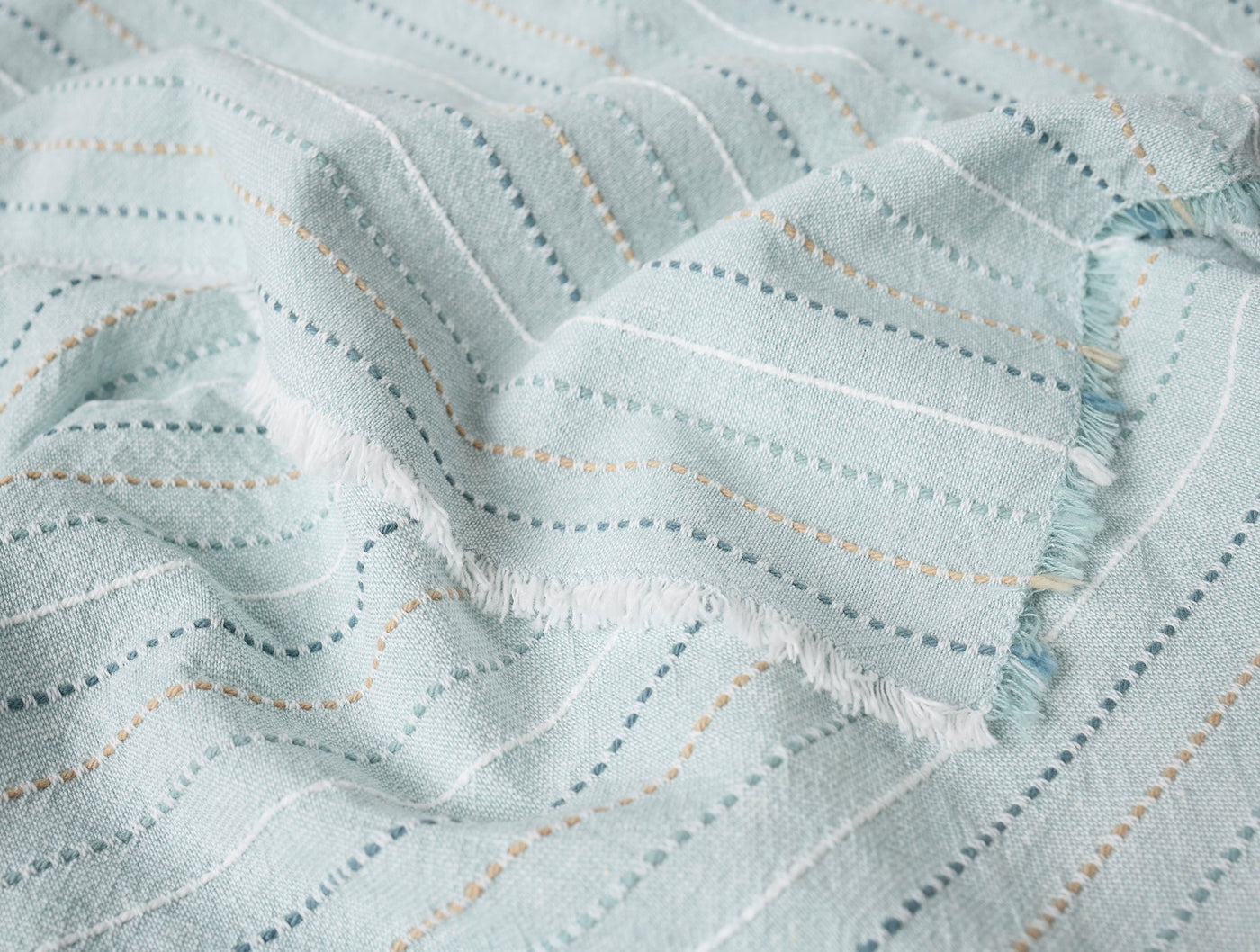 Close-up of Coyuchi Fringe Stripe napkin in mist, showing dotted stripe weave and fringe edge detail.
