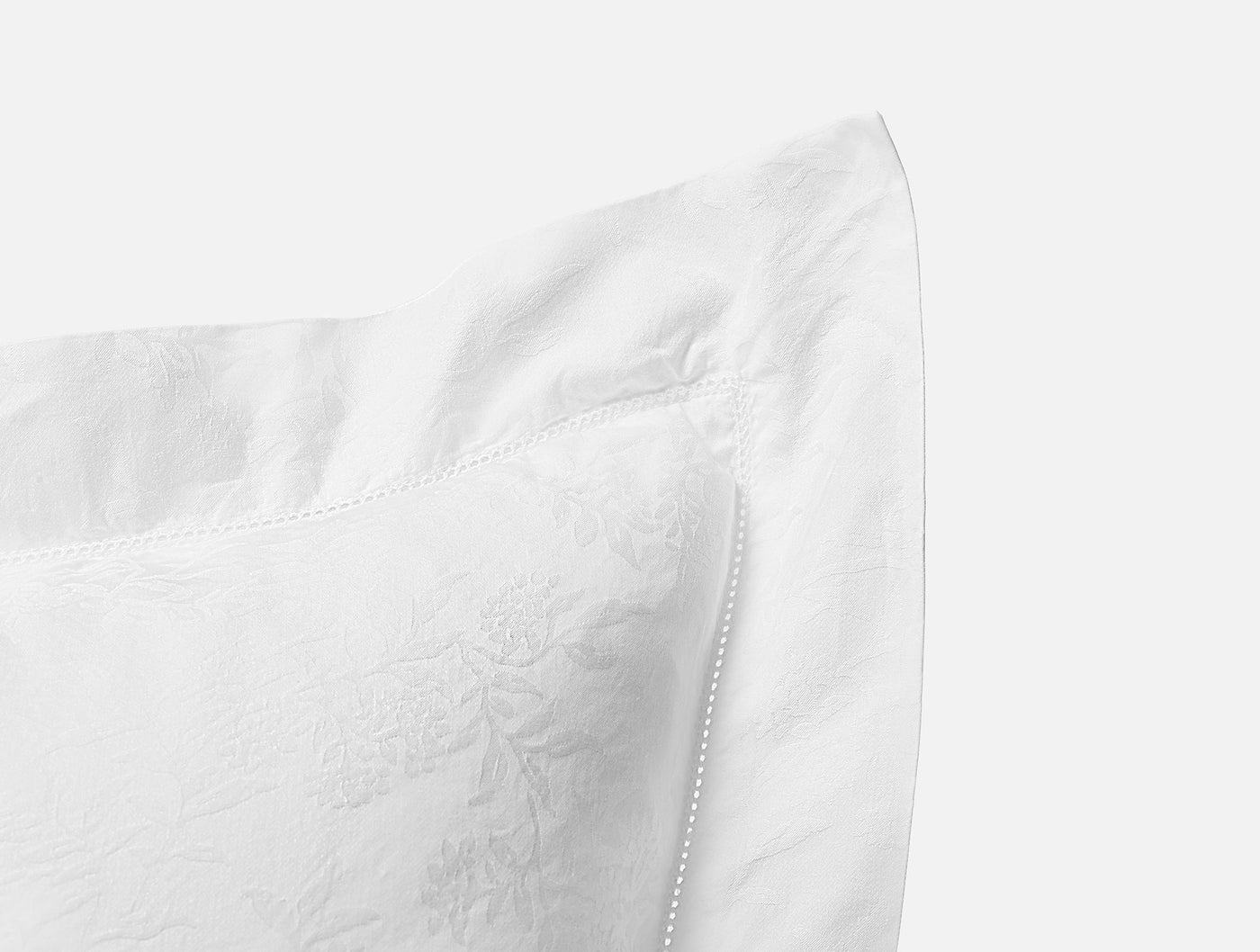 Close-up of white jacquard floral corner detail and hemstitch trim on Coyuchi Heirloom Sateen sham.