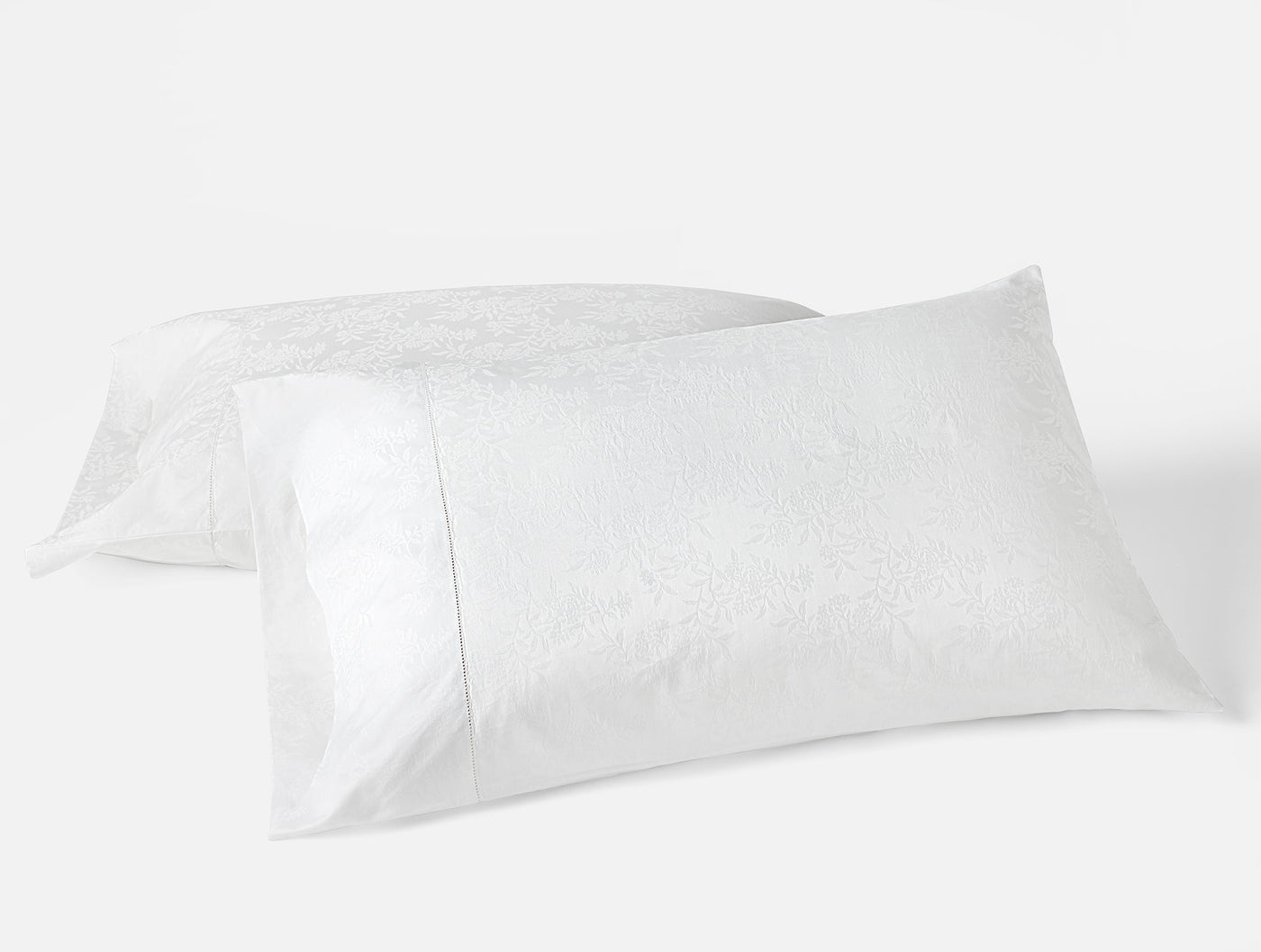 Pair of white Coyuchi Heirloom Sateen pillowcases showing subtle jacquard floral texture.