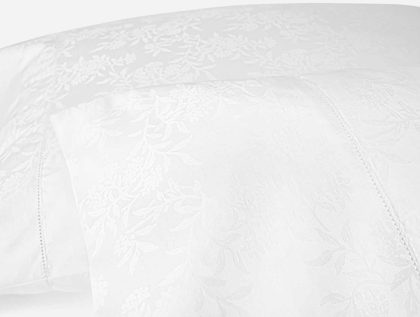 Close-up of white jacquard floral pattern and hemstitch detail on Coyuchi Heirloom Sateen pillowcase.