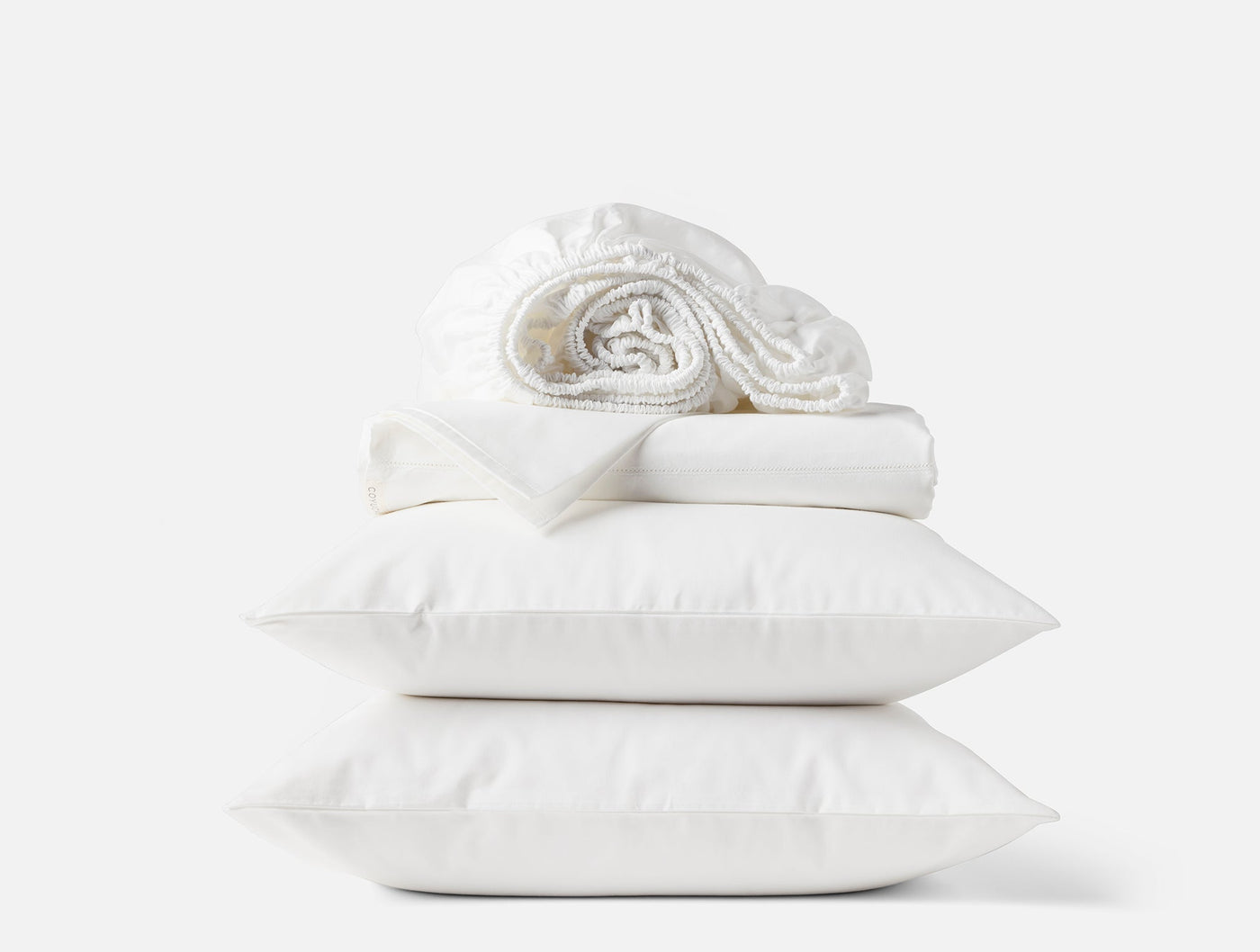Coyuchi Heirloom Sateen sheet set in white, stacked with two pillowcases and rolled sheets.