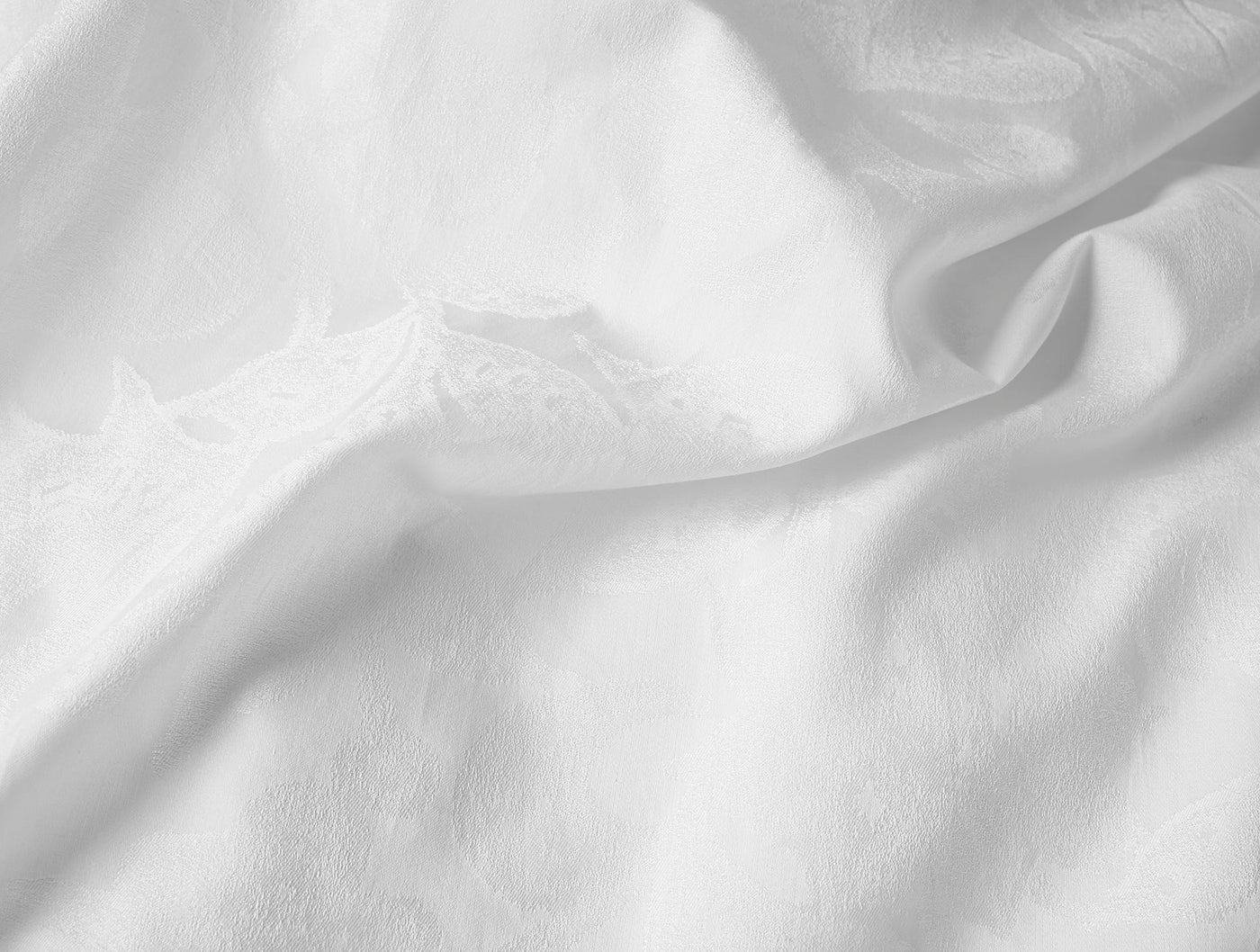 Close-up of white Heritage Percale Jacquard duvet cover showing subtle woven pattern on draped fabric.