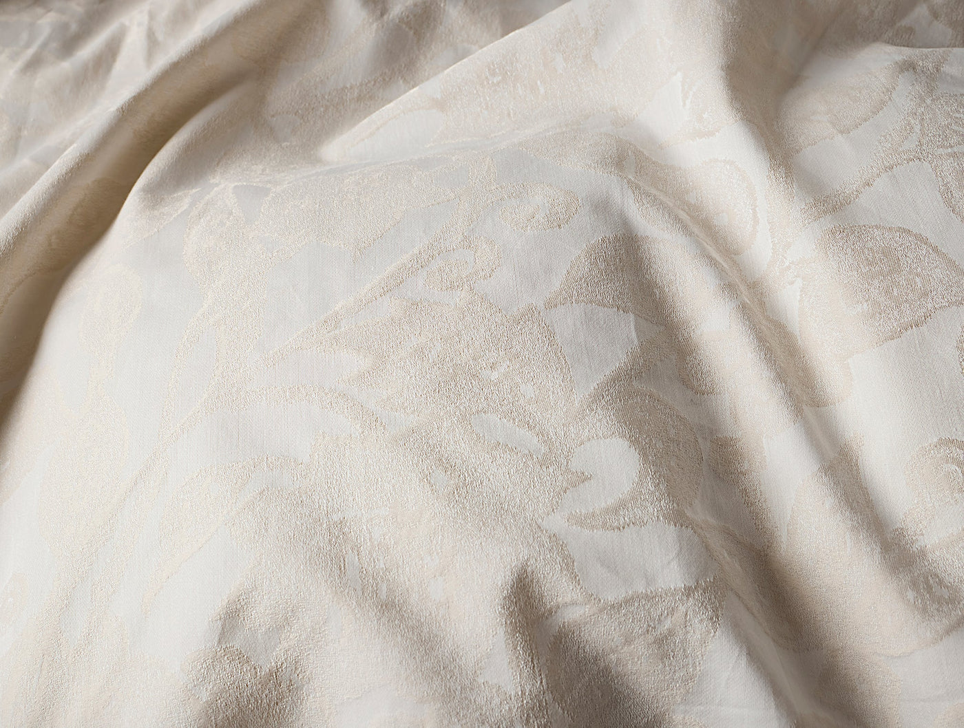 Close-up of ivory jacquard weave with subtle floral pattern on draped Coyuchi Heritage Percale fabric.