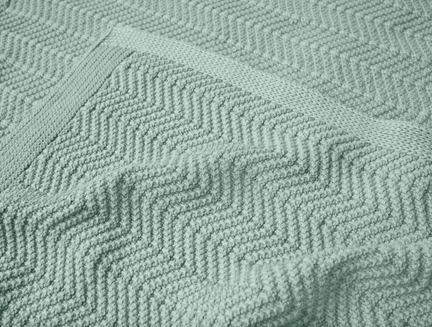Close-up of sage green chevron knit texture on Coyuchi Hermosa throw, showing folded edge.