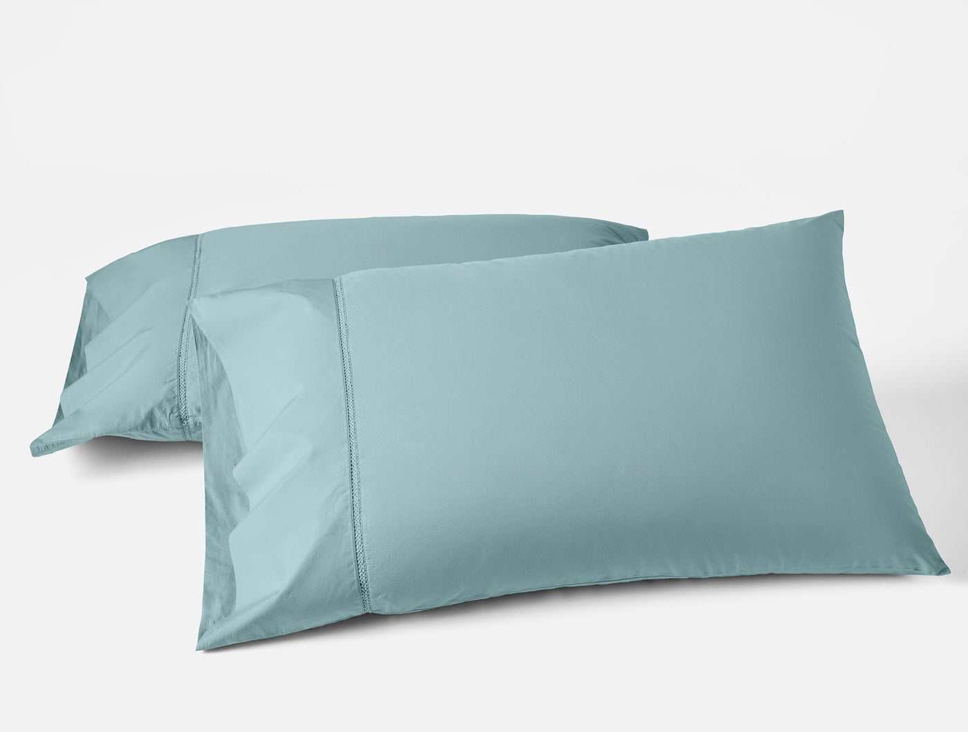 Two Coyuchi Lattice Percale pillowcases in muted teal, stacked at an angle on white background.