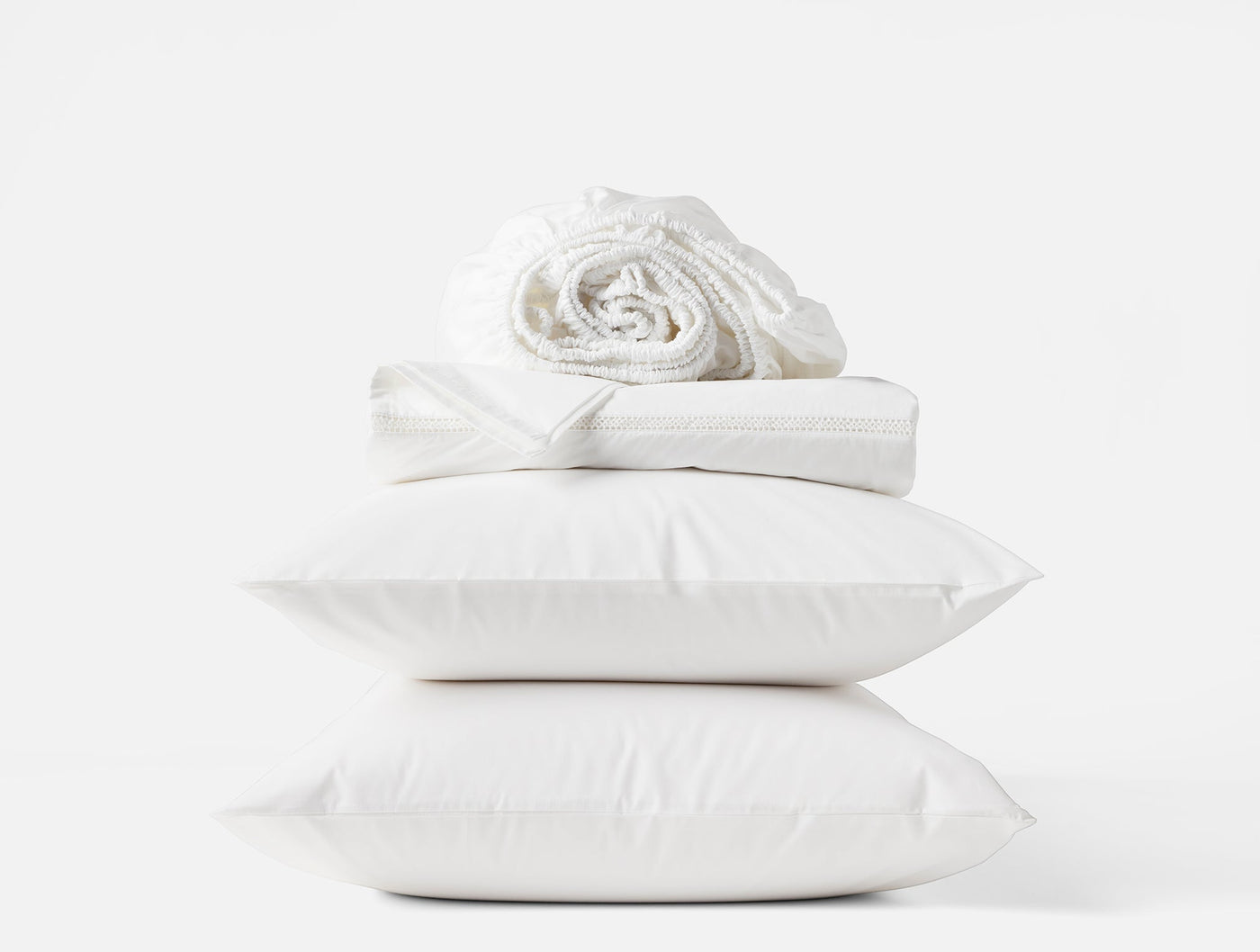 Coyuchi Lattice Percale sheet set in white, stacked pillows with rolled sheets on top.