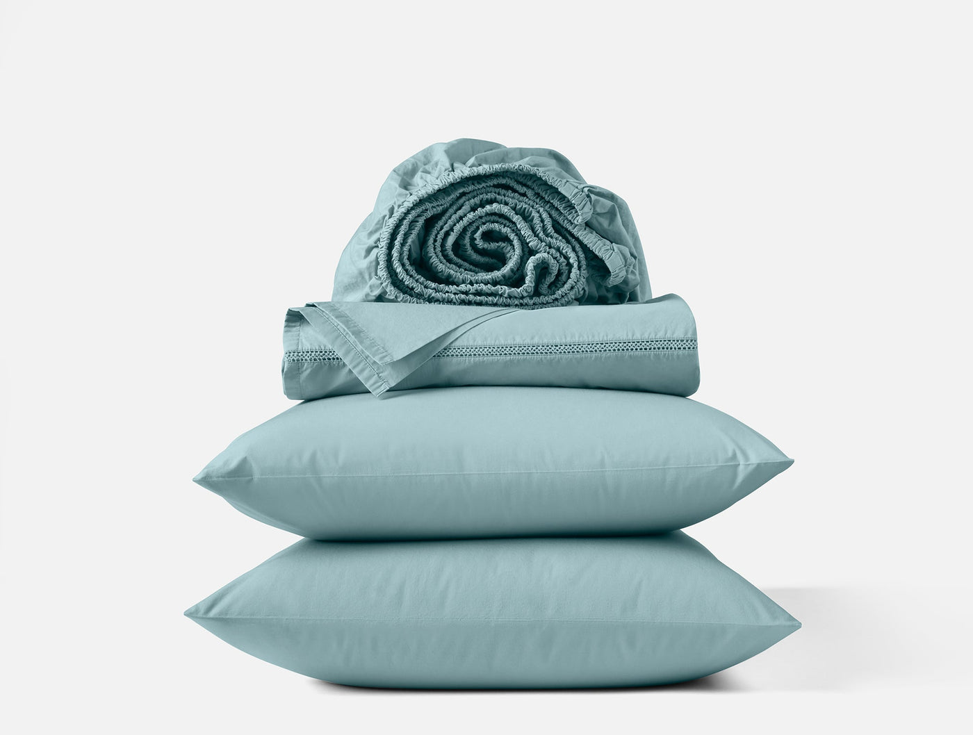 Coyuchi Lattice Percale sheet set stacked with rolled fitted sheet on top, seafoam.