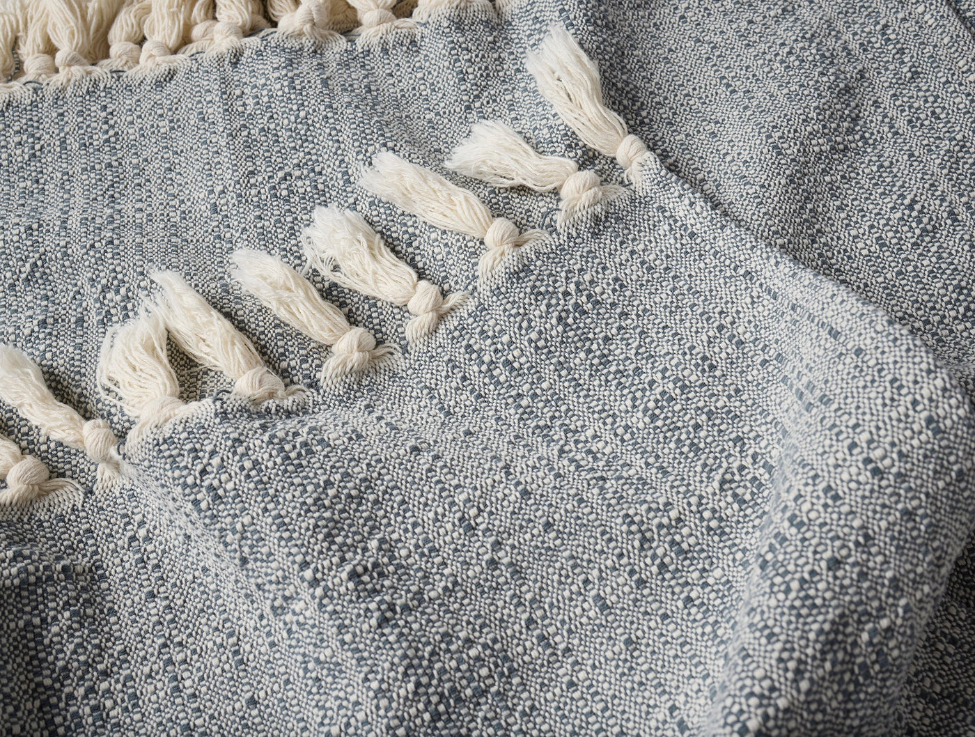 Close-up of Coyuchi Lido throw's woven slate texture with ivory tassel trim detail.