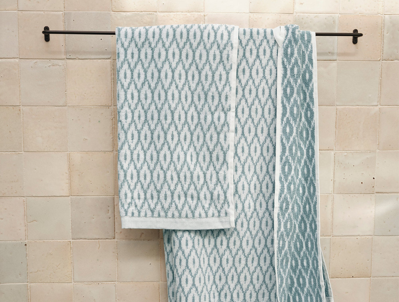 Coyuchi Stinson hand towels in sage geometric jacquard pattern, draped on iron towel bar.