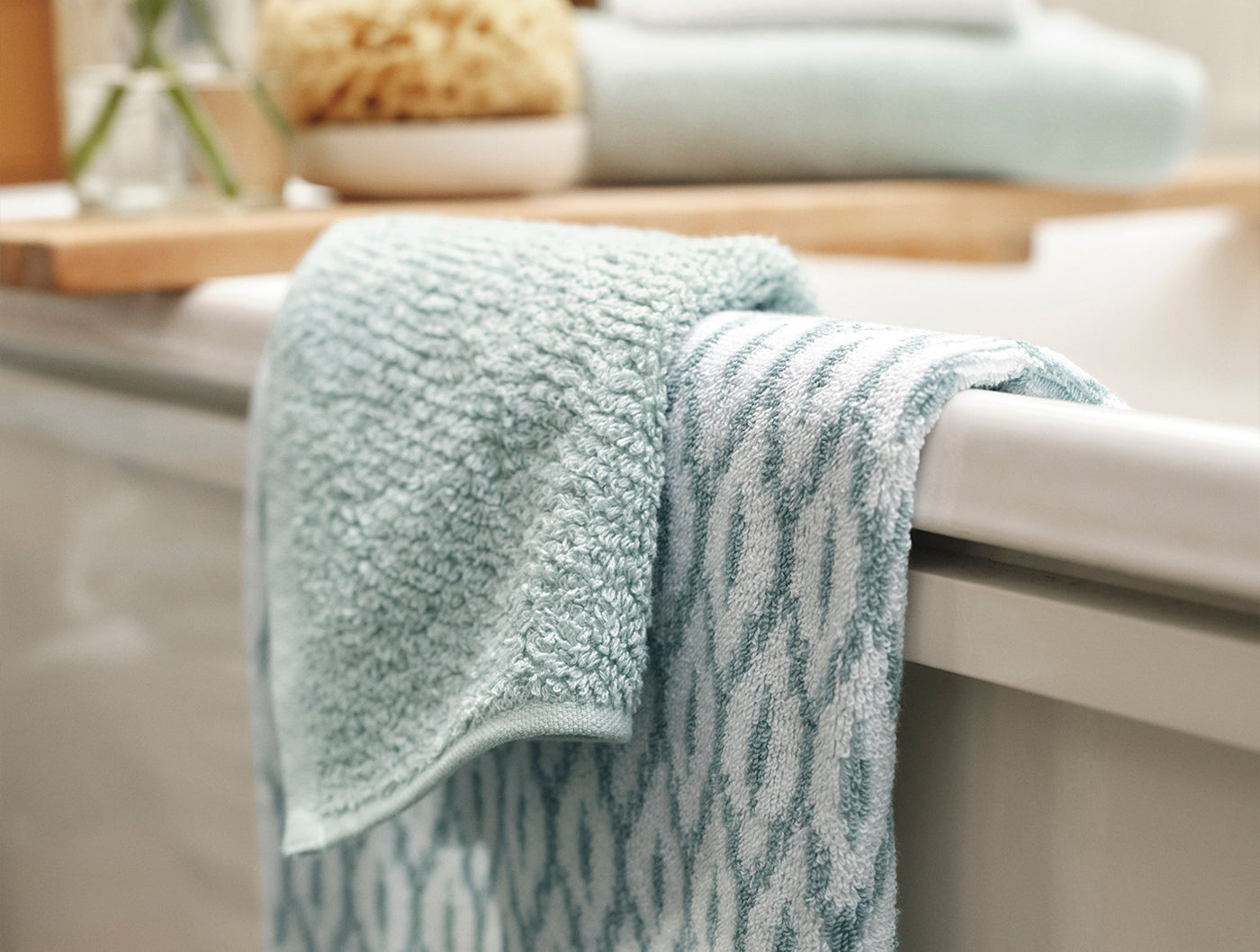 Coyuchi Air Weight bath sheet in seafoam, draped over tub edge showing wave texture detail.
