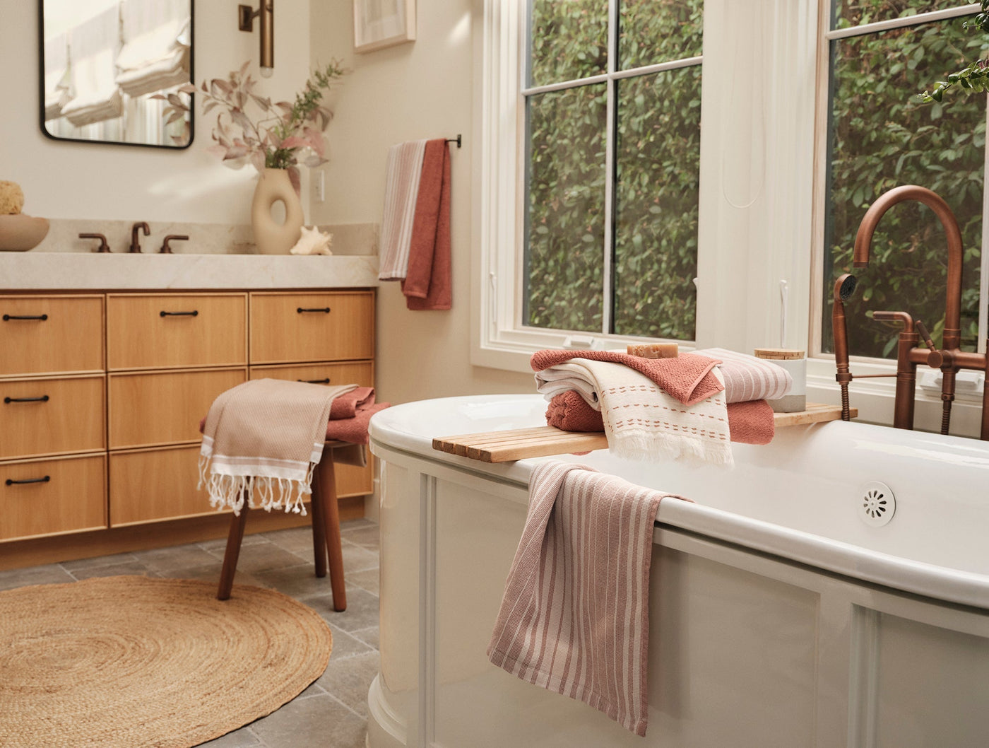 Blush pink hand towel draped over a freestanding bathtub in a bright, neutral bathroom.