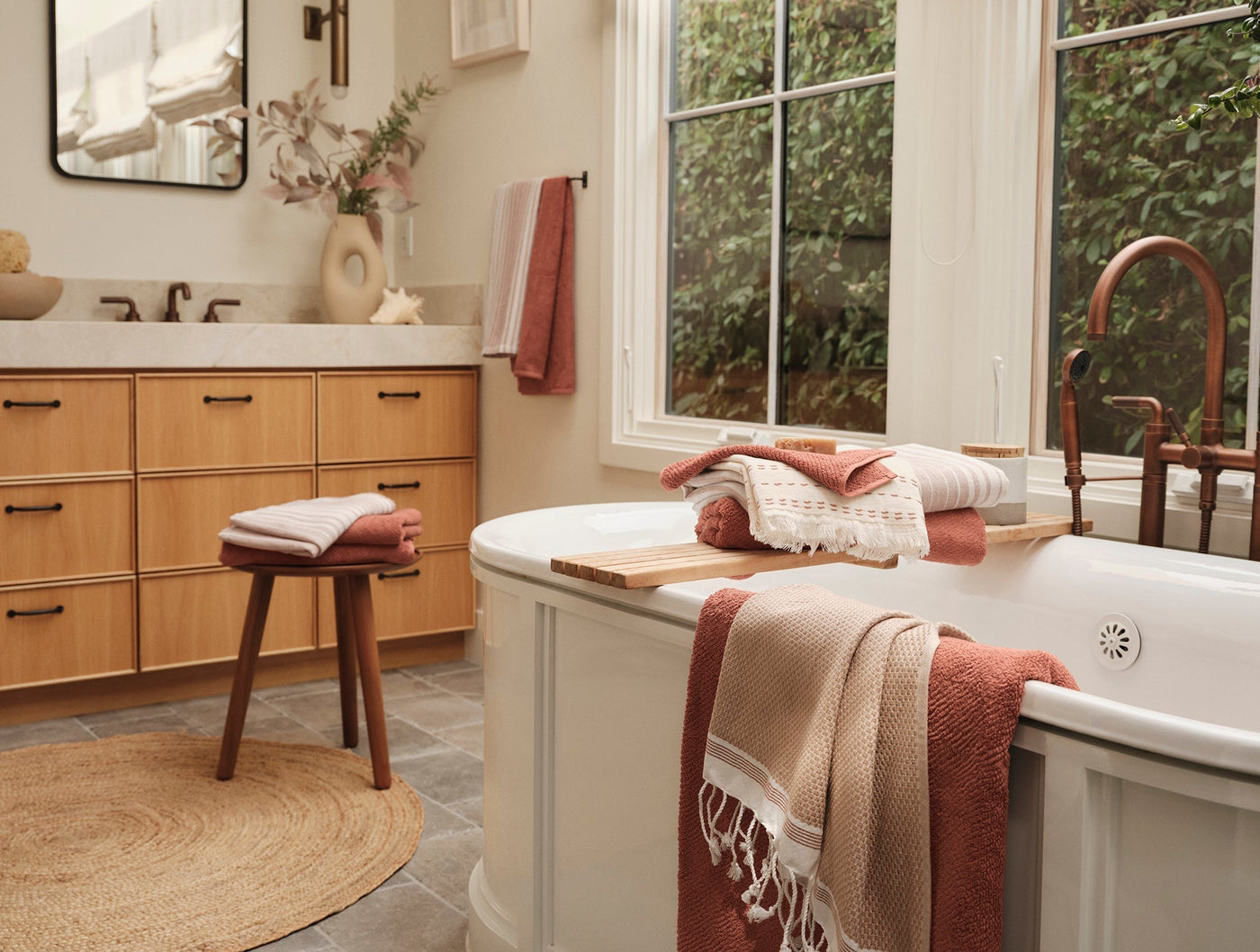 Coyuchi Mediterranean towels in terracotta and blush styled on bathtub and stool in bright bathroom.