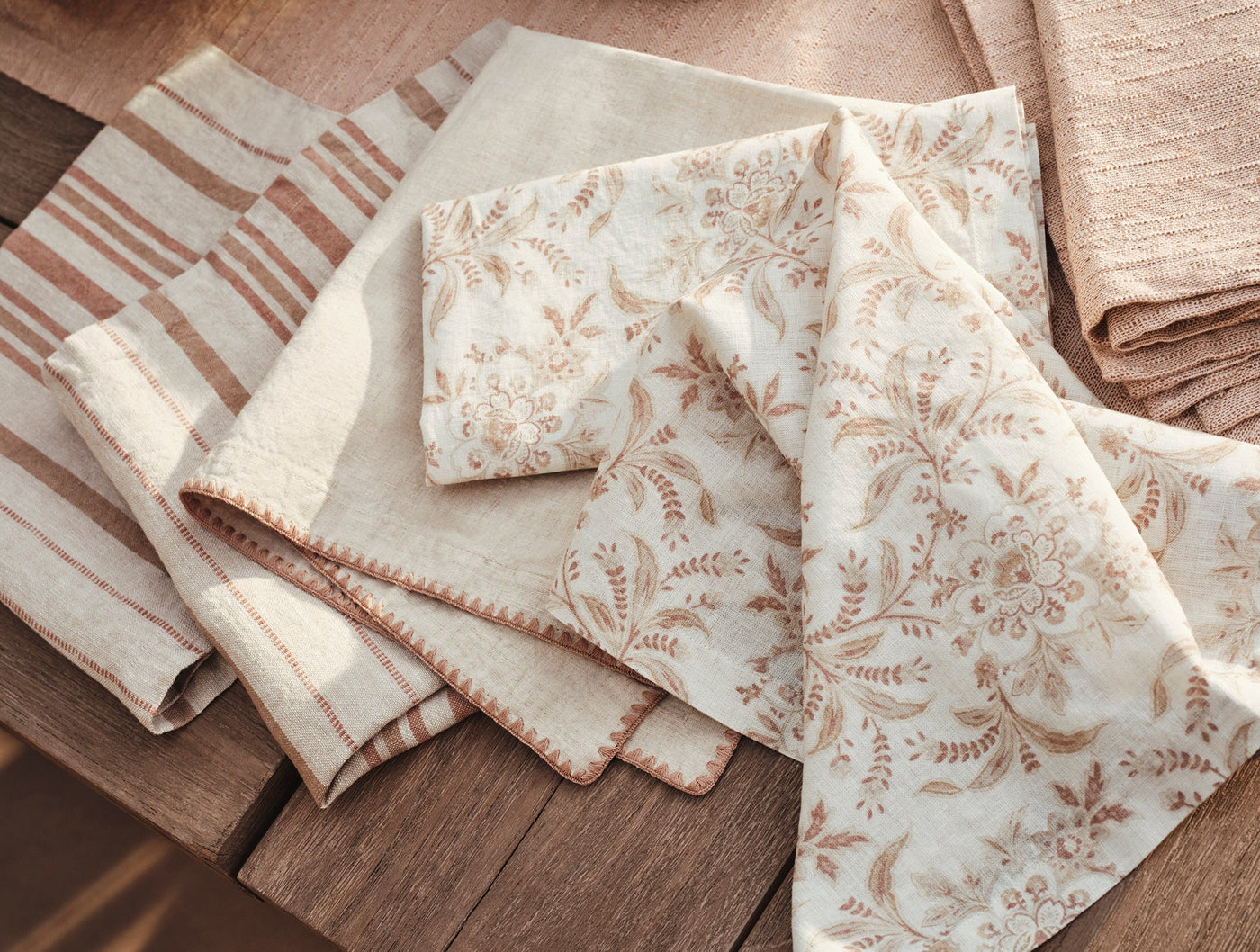 Coyuchi Marguerite Print napkins fanned on wood surface, floral print beside striped ivory linen.