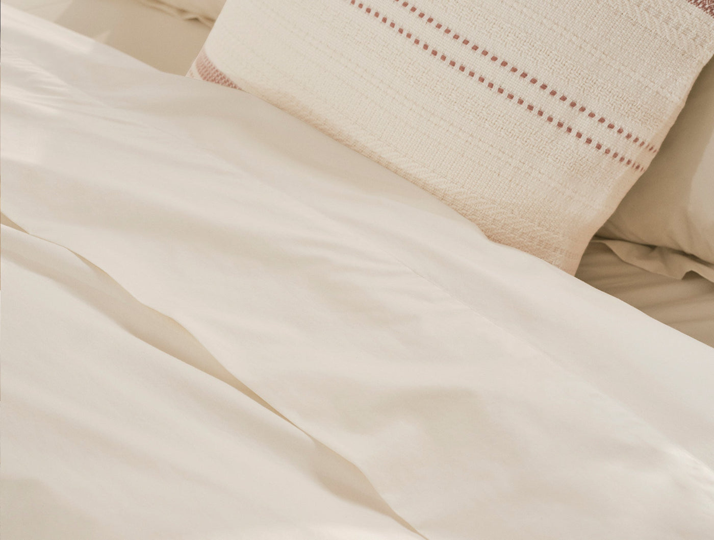 Close-up of ivory Coyuchi Refined Percale duvet cover with textured woven pillow in background.